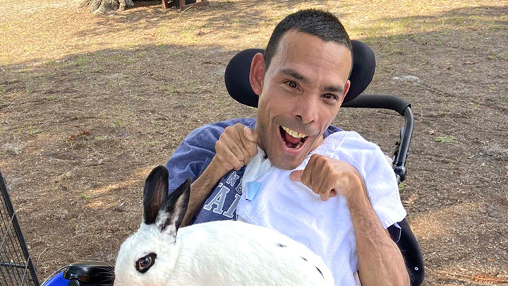 Bruce, seated in his wheelchair, smiles at the camera with a large bunny resting on his lap.