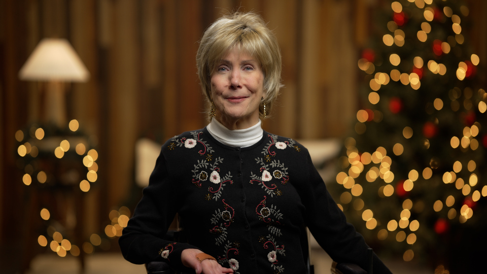 Joni Eareckson Tada smiling for the camera. Behind her are Christmas tree and Christmas lights.
