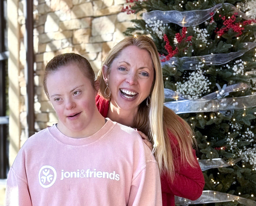 Shauna smiles with her daughter Sarah, who has Down syndrome, in front of a Christmas tree.