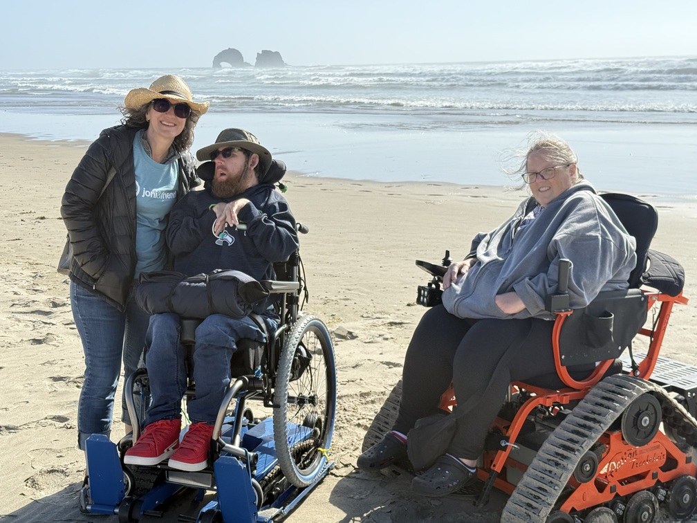 Alex and Trish on a beach with another woman who is using a wheelchair.