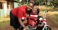 A mother poses for a photo next to her child, smiling in a new wheelchair