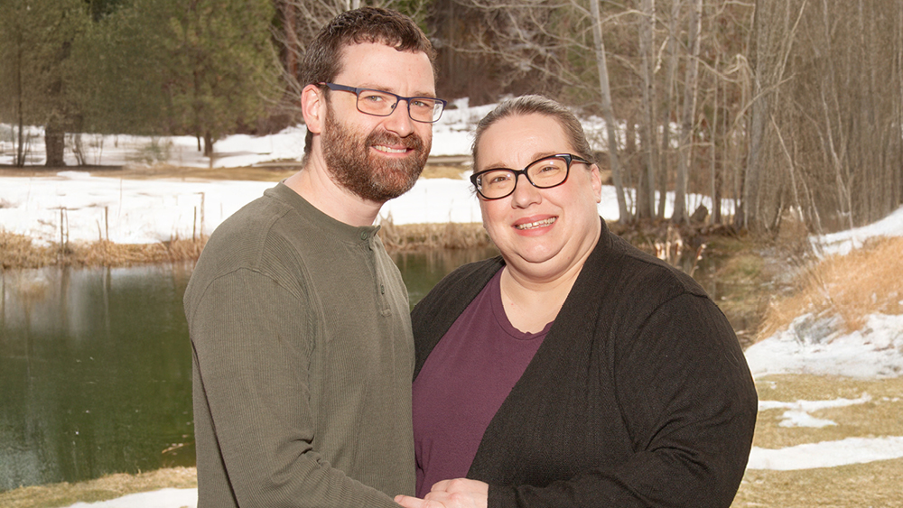 A couple poses for a photo in front a pond in the woods