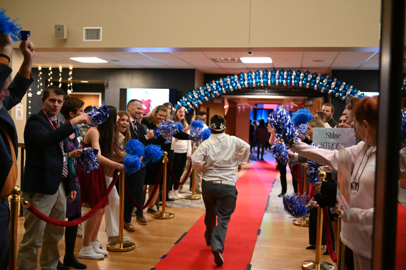 A man walking down the middle of a red carpet while people on both sides cheer him.