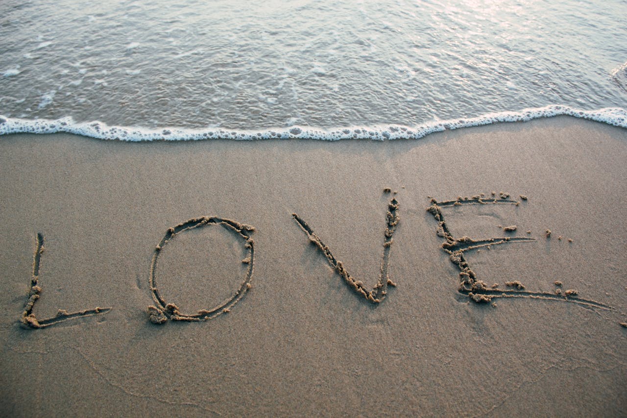 The word "LOVE" written in beach sand as water approaches.