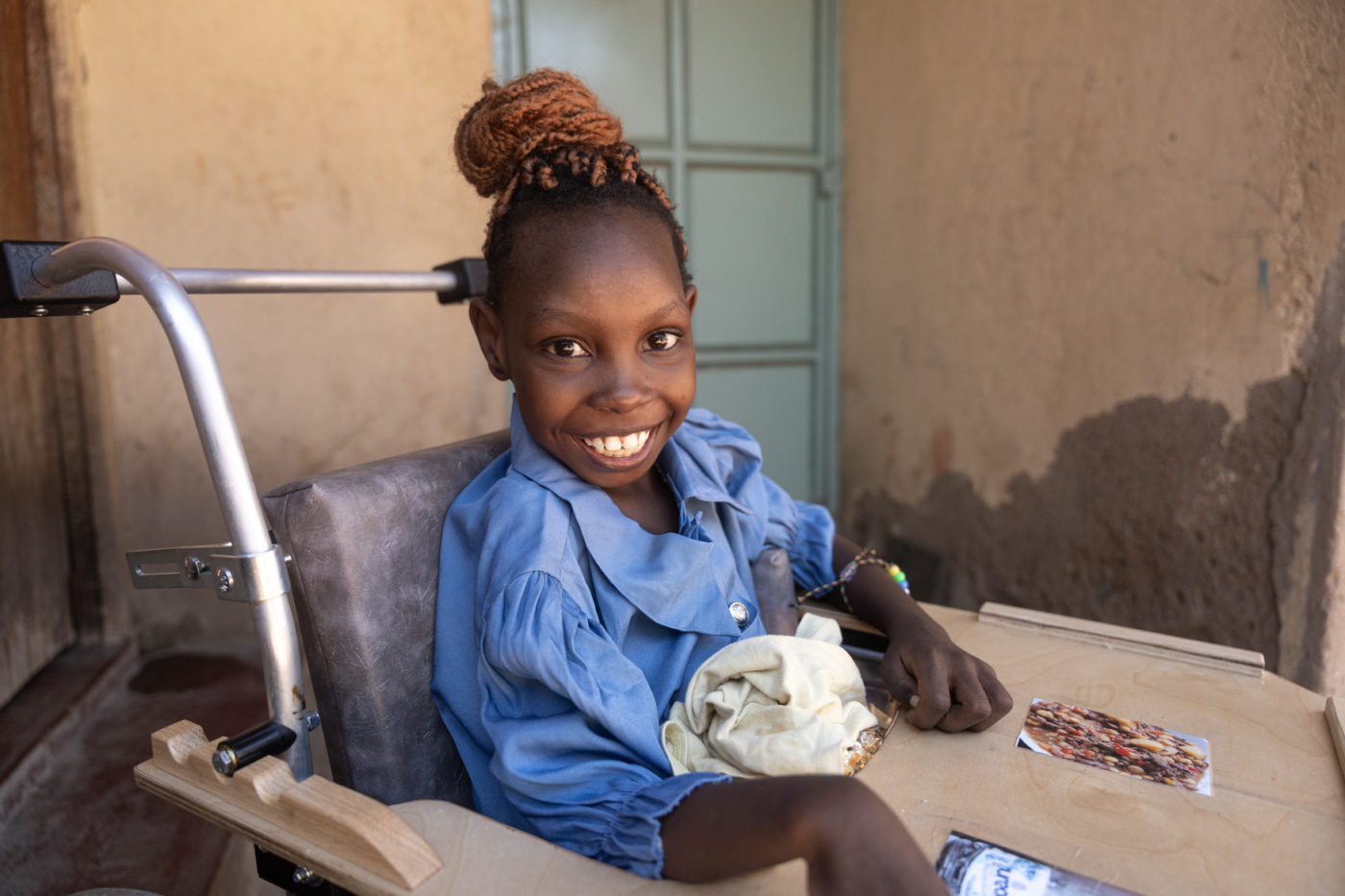 Praise smiling widely for the camera while sitting in her wheelchair.