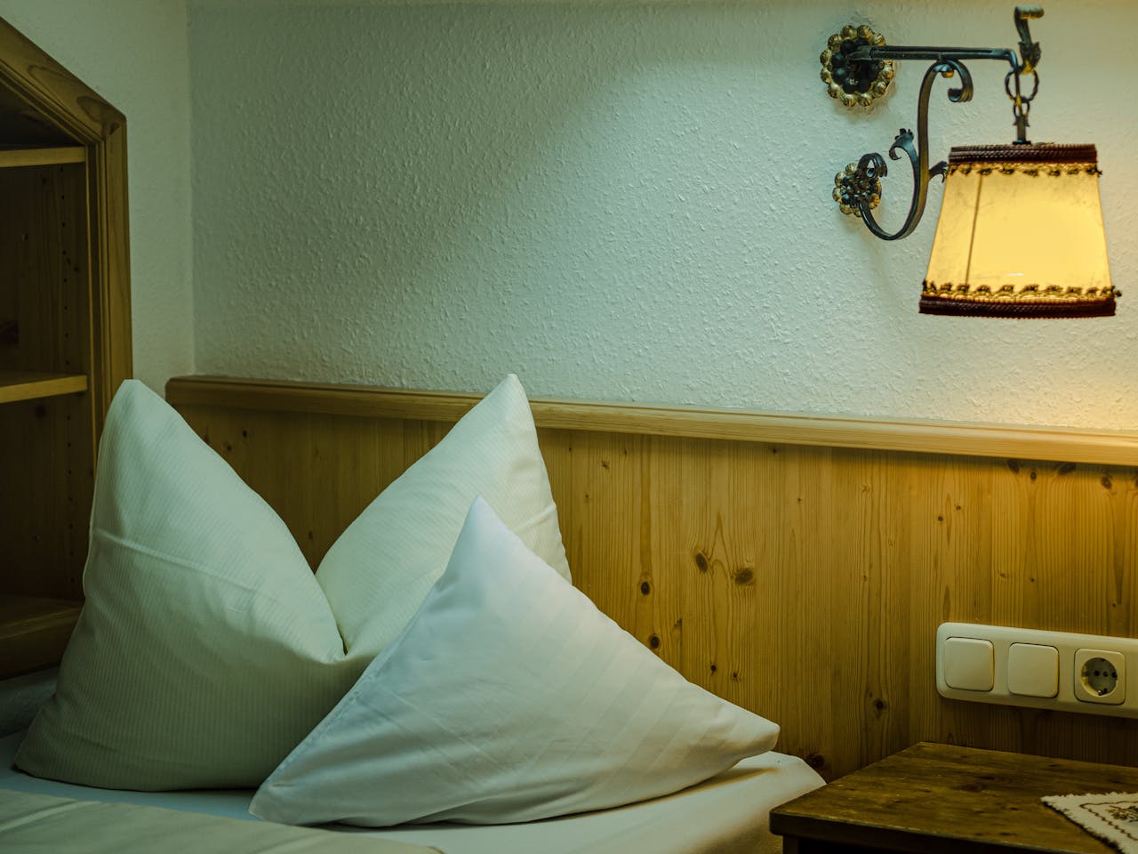 Pillows on a bed beside a wall lamp.