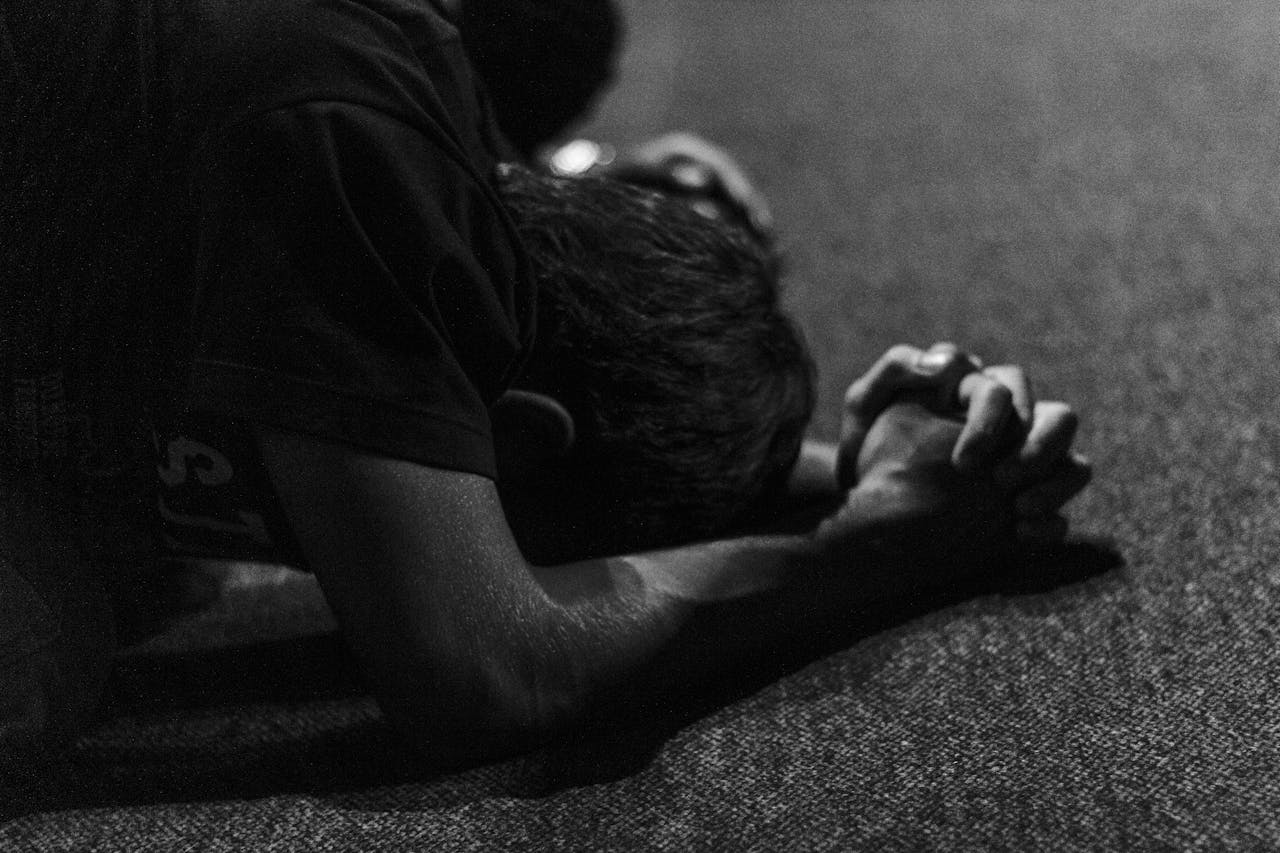 A man praying with his hands on the floor and his hands clasped together.