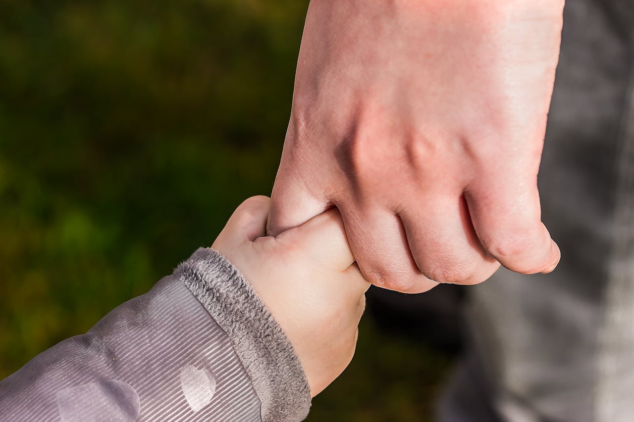 A child holding tightly the pinky finger of an adult.
