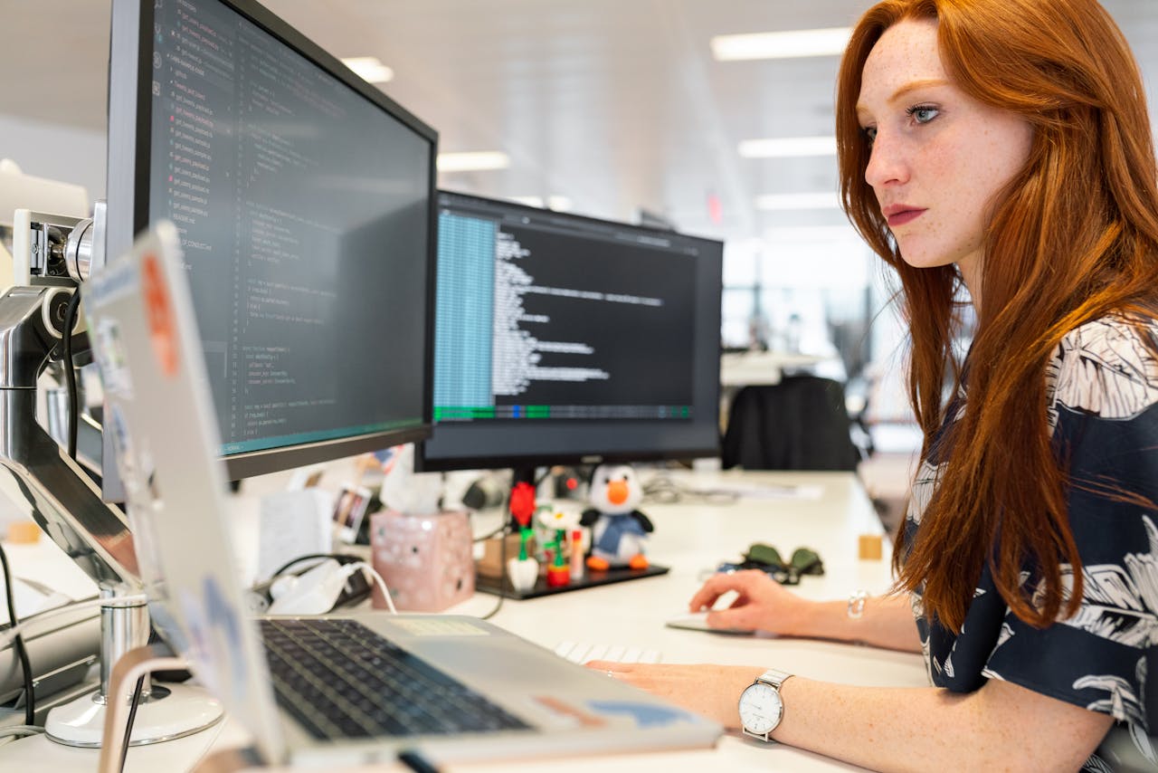 A woman concentrating while working in front of several computer screens.