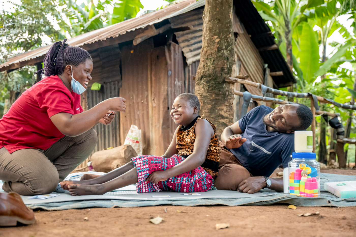 A boy sitting on a floor mat with a woman in front of him and a man behind him.