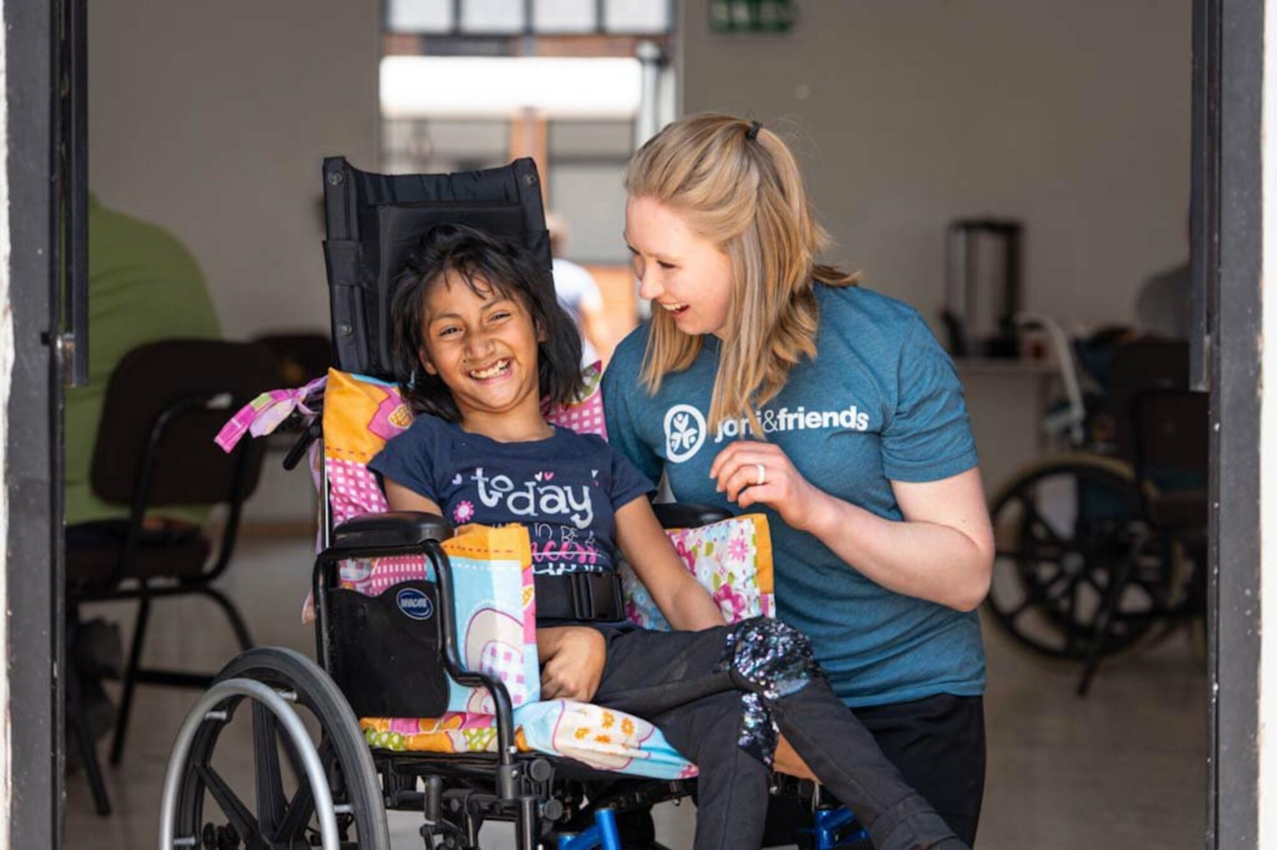 A Joni and Friends staff member and a girl who uses a wheelchair smiling and enjoying the moment together.
