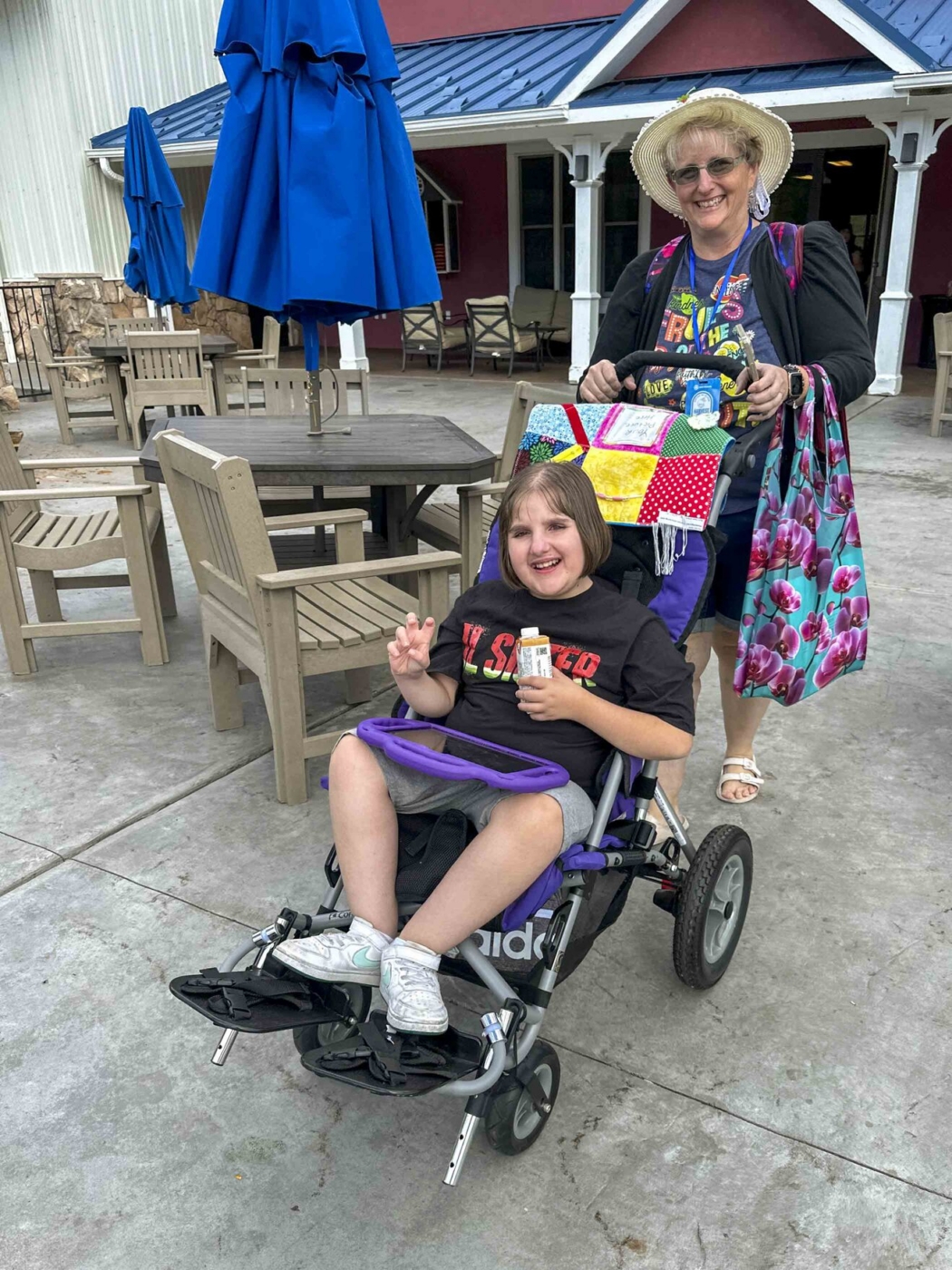 Andi sitting in a stroller, smiling, while a woman pushes her and also smiles at the camera.