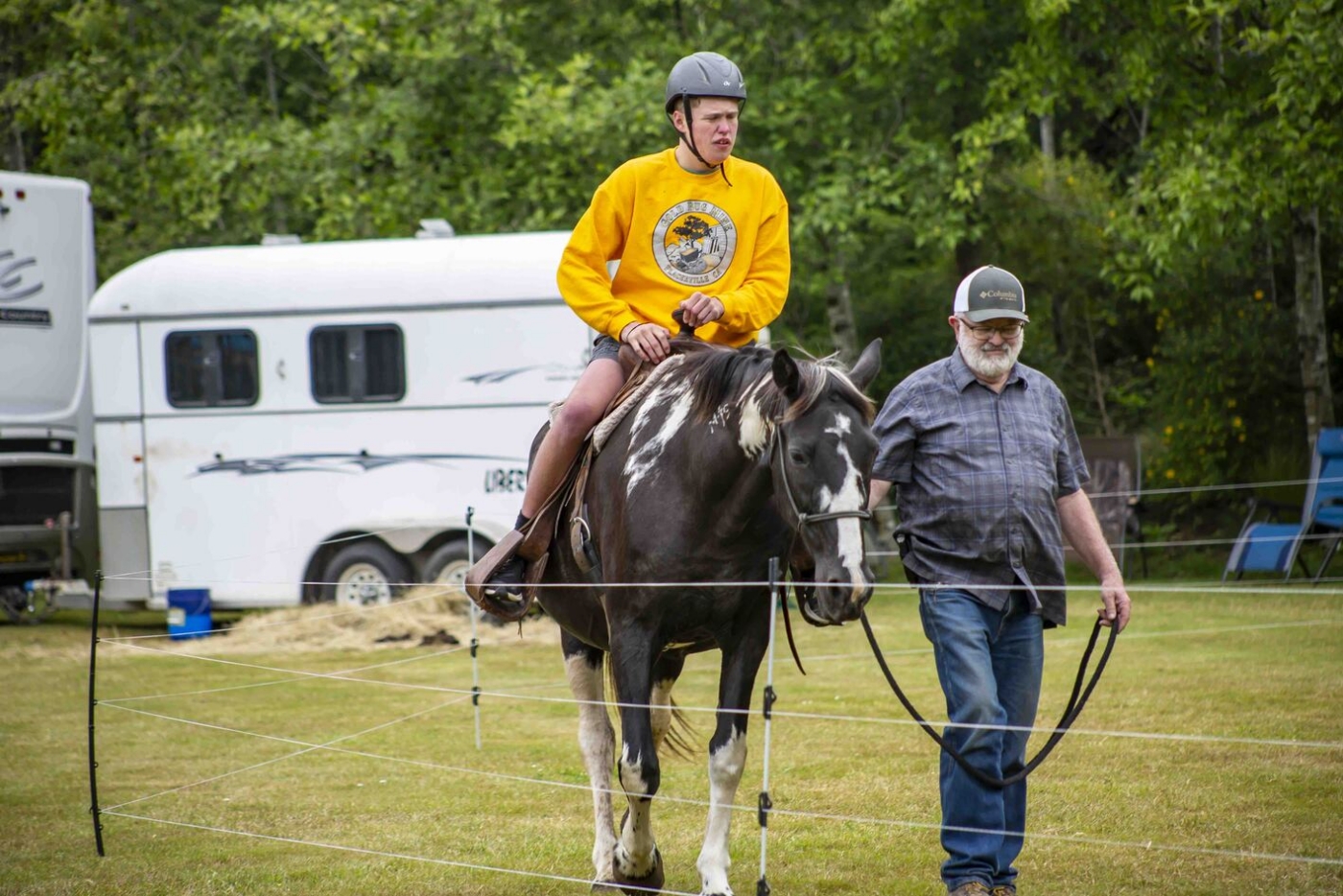 Simon rides a horse while a man guides the horse.