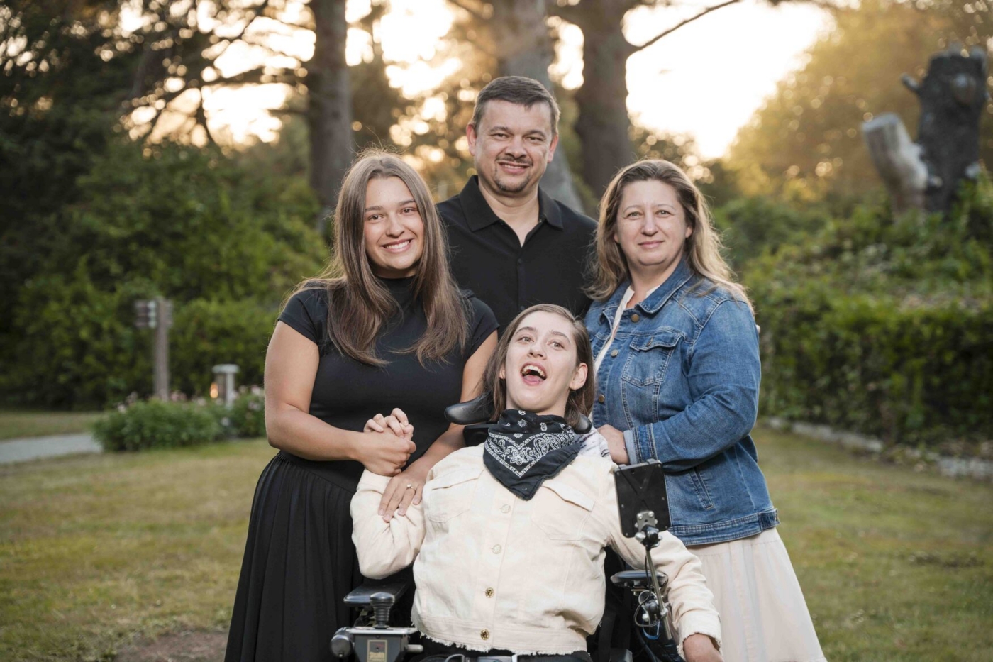 Sophia sits in her wheelchair with her mom, dad, and another woman, all posing and smiling for the camera.