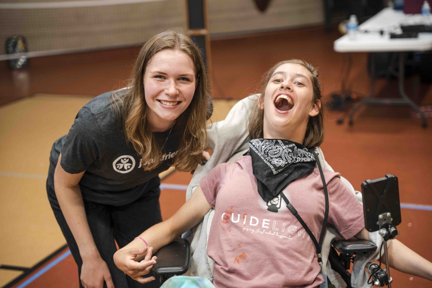 Sydney stands next to her buddy, who uses a wheelchair. Both are smiling widely at the camera.