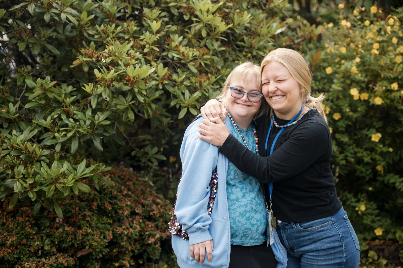 A woman with Down Syndrome is hugged by her buddy at Family Retreat. Both are smiling and posing for the camera.