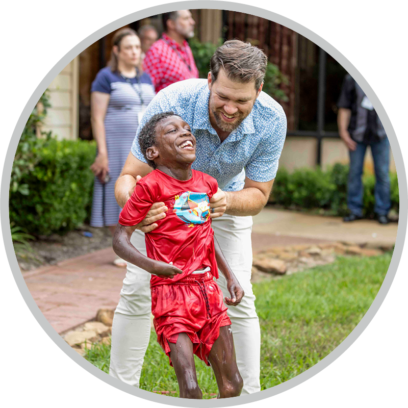 A boy stands with his dad who is assisting him, and both are smiling.