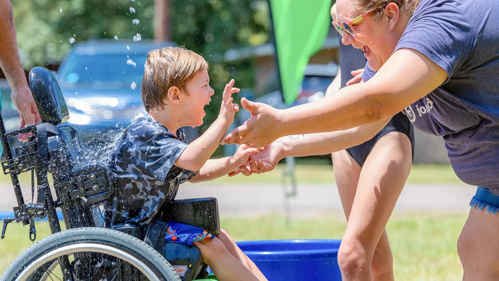 A child in a wheelchair joyfully gets splashed by water