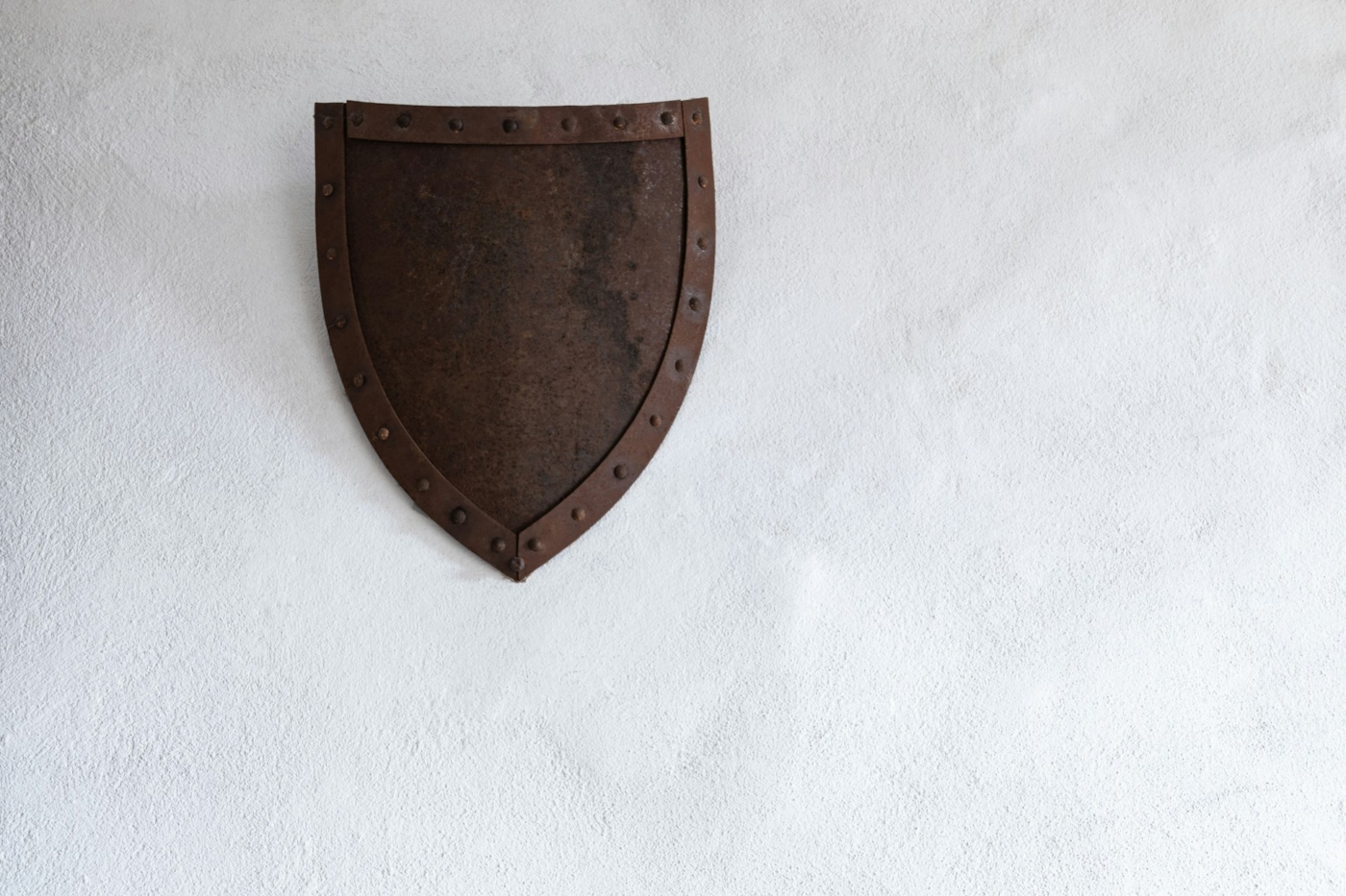 Vintage metal heater shield made of dark, rusted metal with a riveted border, displayed on a white textured wall.