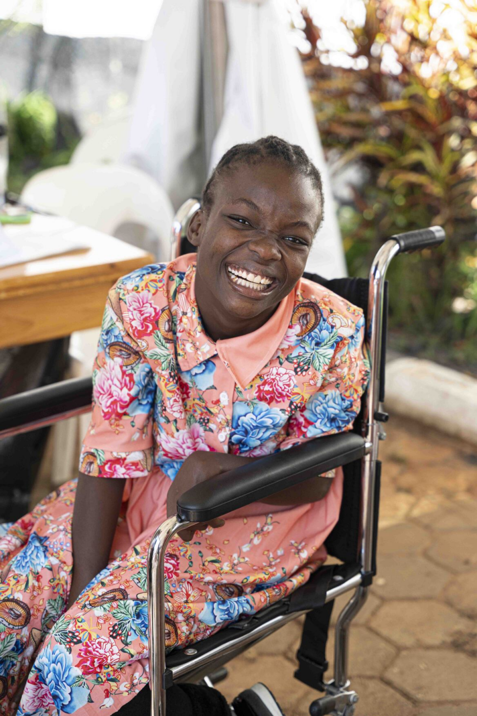 Mapalo sits in a wheelchair, smiling widely at the camera.