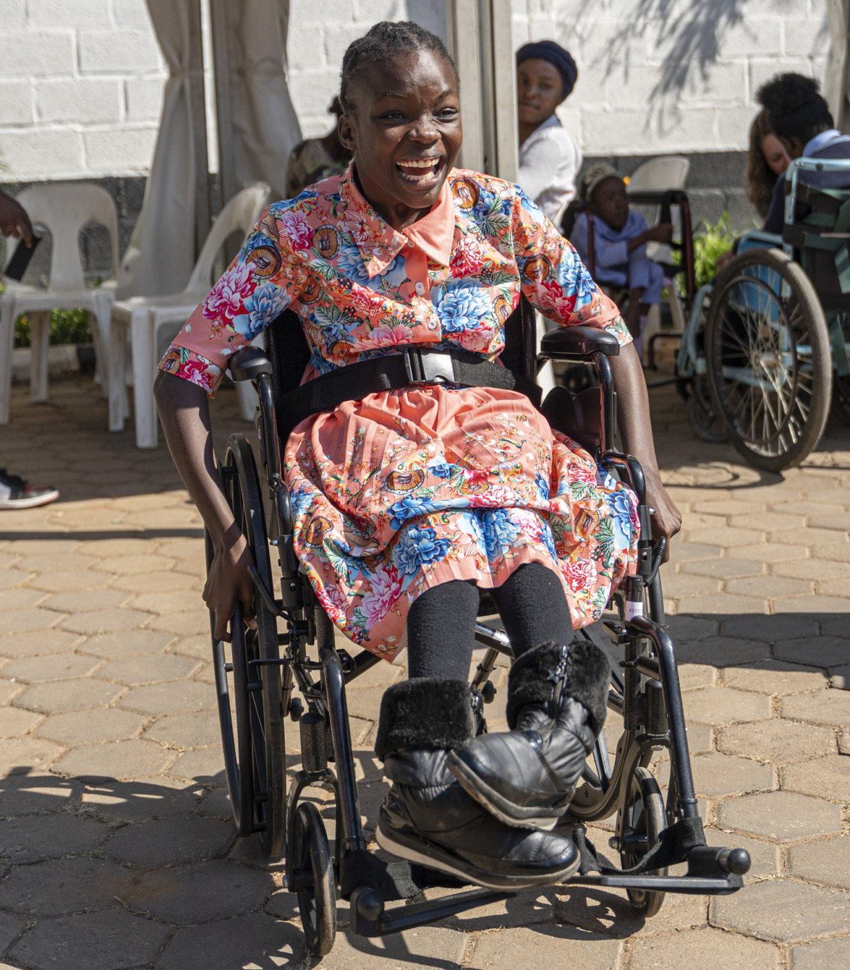 Mapalo, seated in her new wheelchair, propels herself forward with a joyful expression.