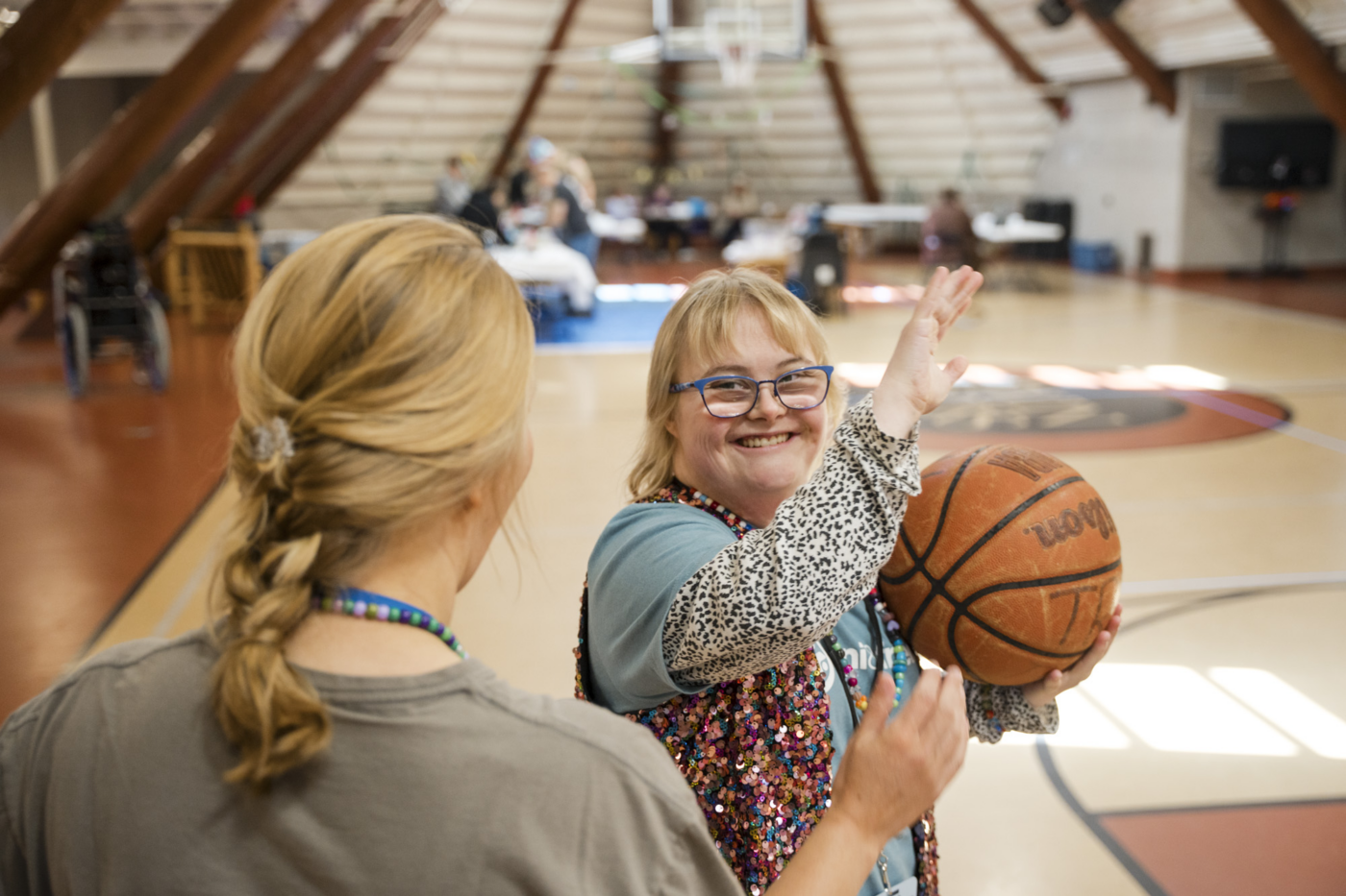 Emily, a woman with Down syndrome, gives a high five while holding a basketball.