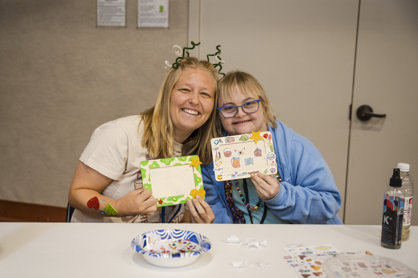 Katie and Emily sit next to each other, showing their artwork.
