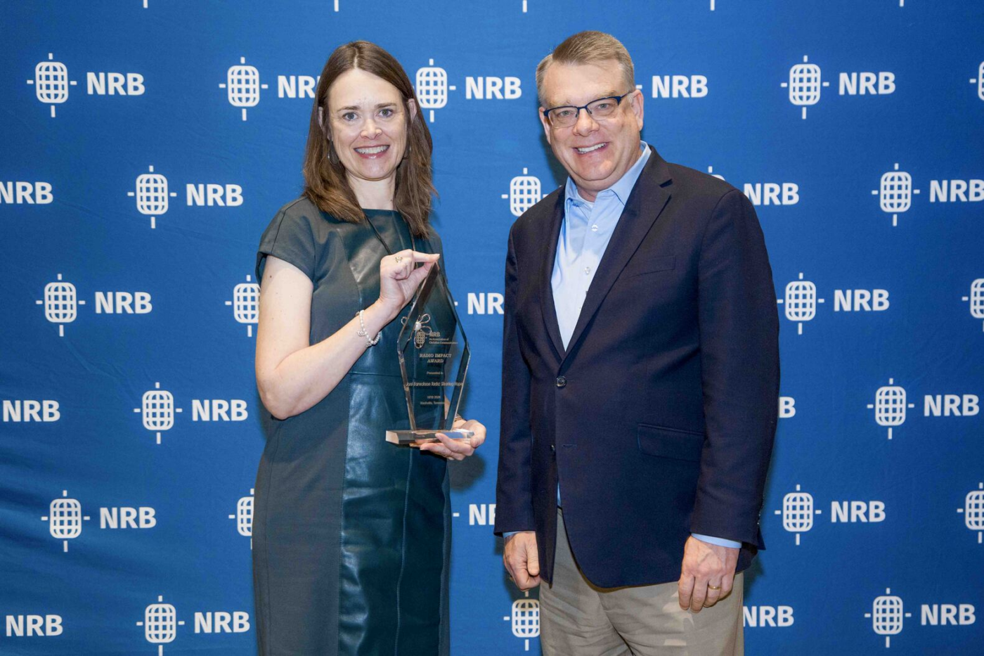 Catherine Cobb holding the National Religious Broadcasters Radio Impact Award while Shawn Thornton stands beside her. Both smile and pose in front of an NRB backdrop.