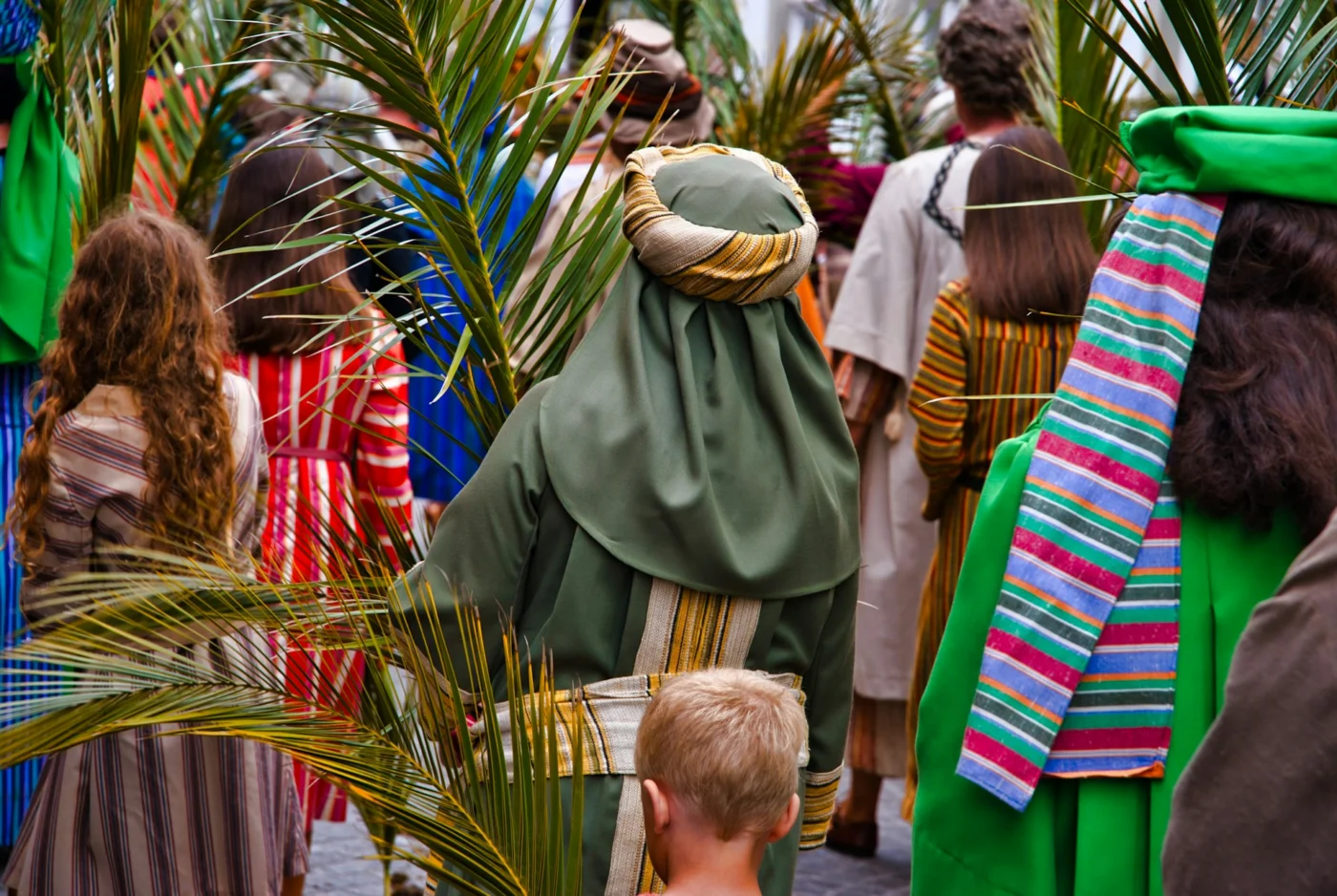 People seen from behind holding palm branches while waiting for someone.