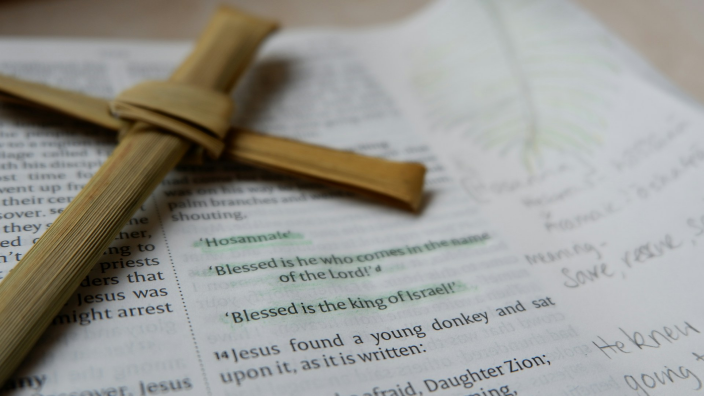 A cross resting on an open Bible showing the verse Hosanna Blessed is he who comes in the name of the Lord Blessed is the king of Israel