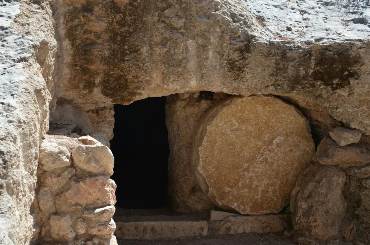 A rock-cut tomb with a prominent large, circular stone rolled to the side of the entrance.