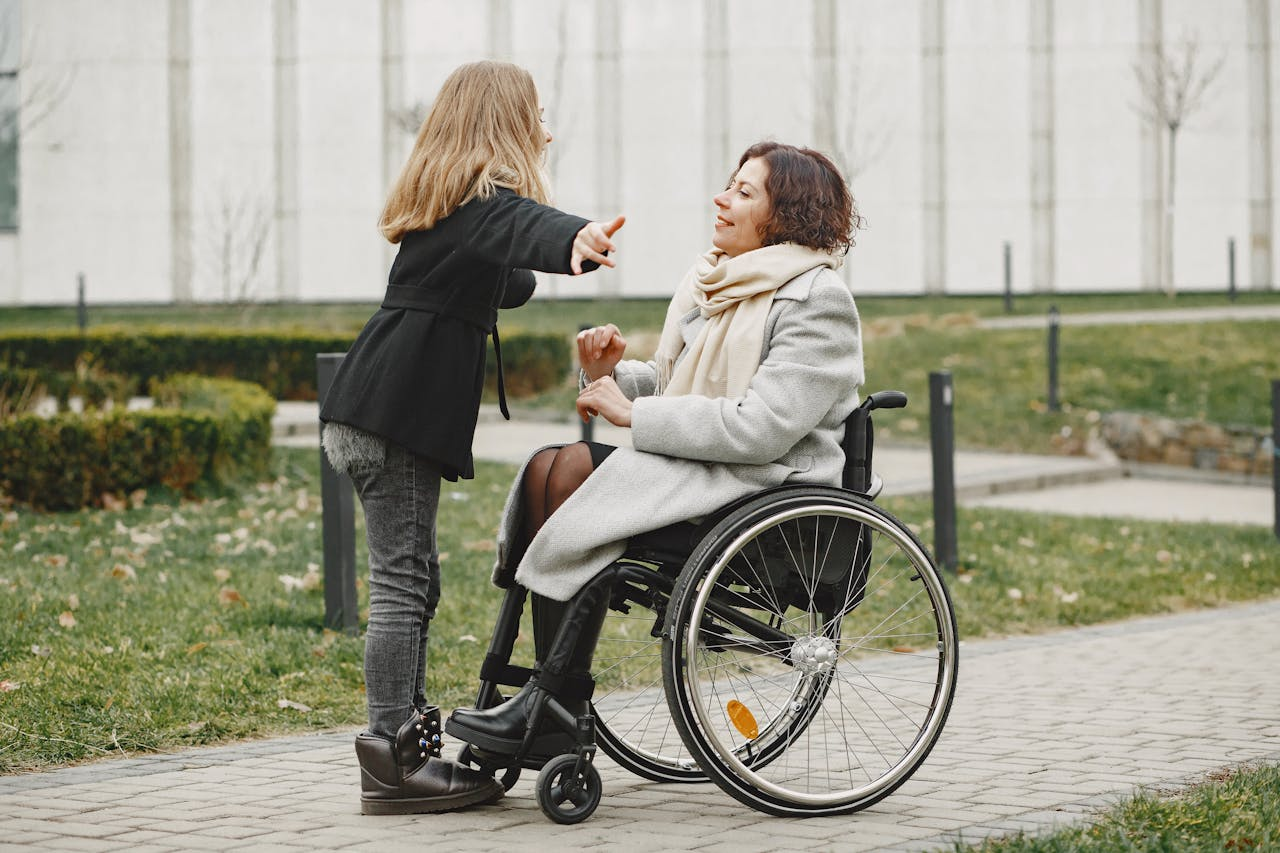 A young girl with arms wide open reaching to hug a woman in a wheelchair.