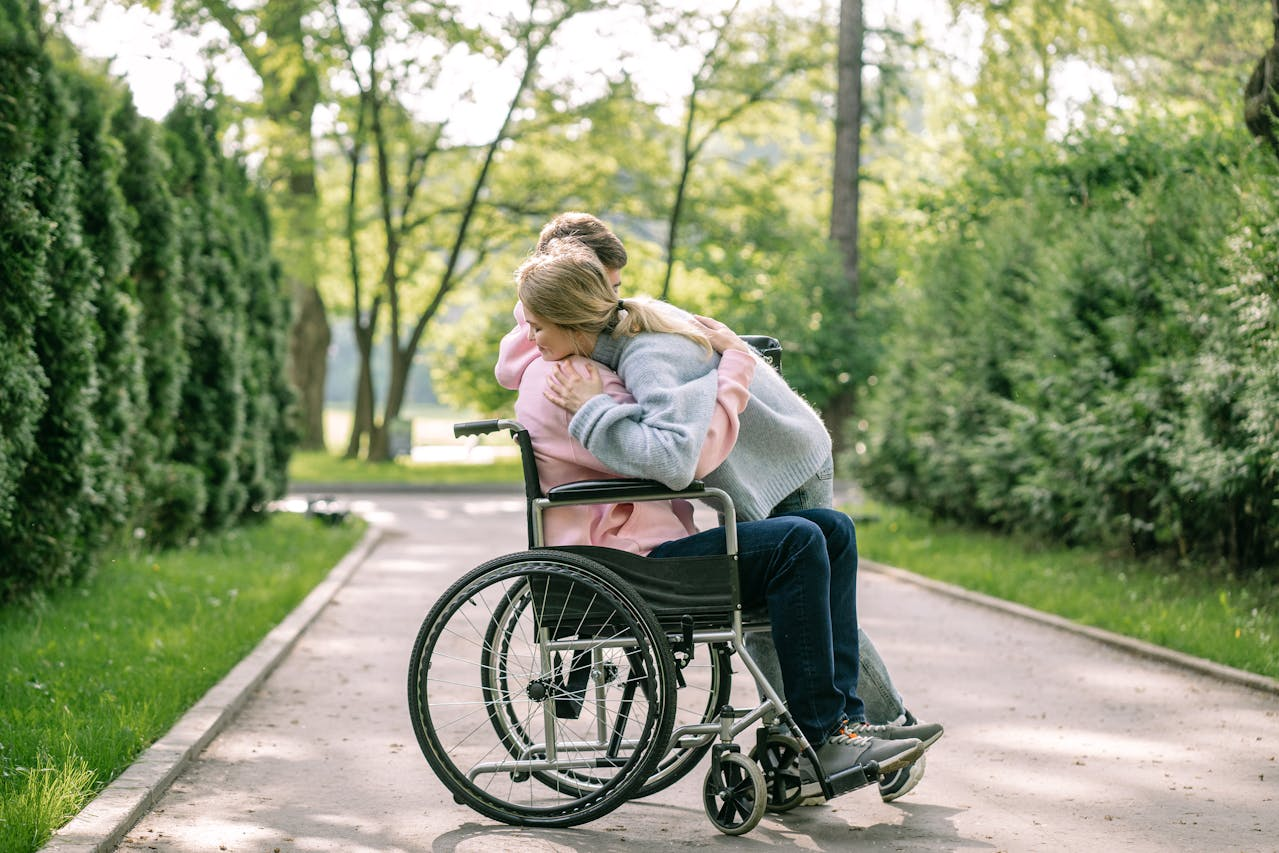 A quiet moment in a park with a person seated in a wheelchair being embraced by another individual. 