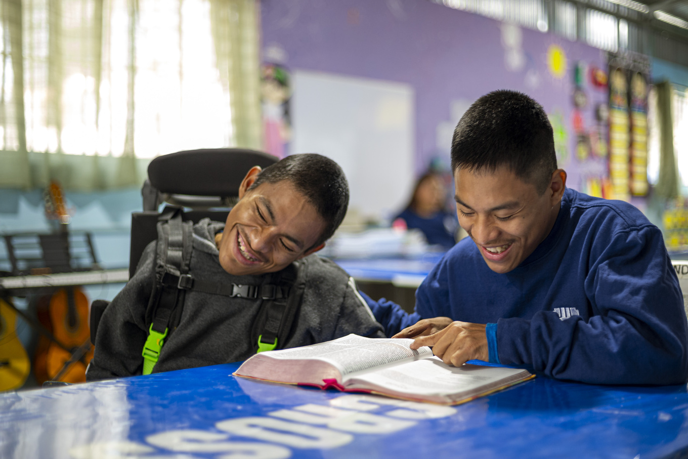 Kevin next to his brother Manual who is in a wheelchair with a Bible open in front of them.