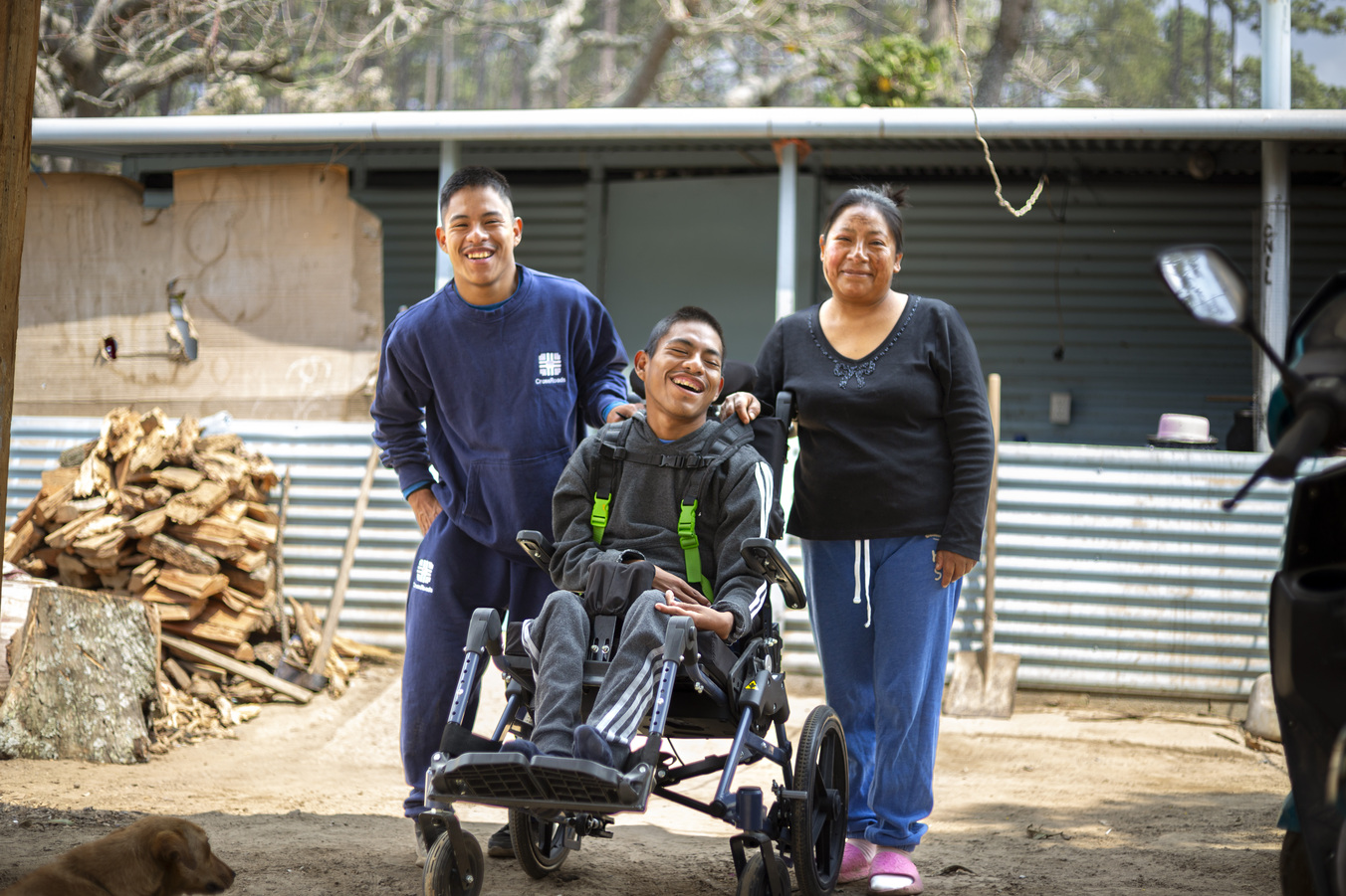Kevin, Manuel with his new wheelchair and their mom Anna. All are smiling and posing for the camera.