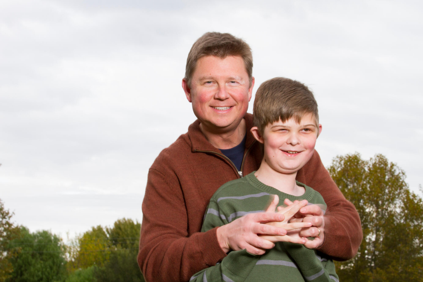 Steve Bundy is hugging his son Caleb while both are smiling and posing for the camera.