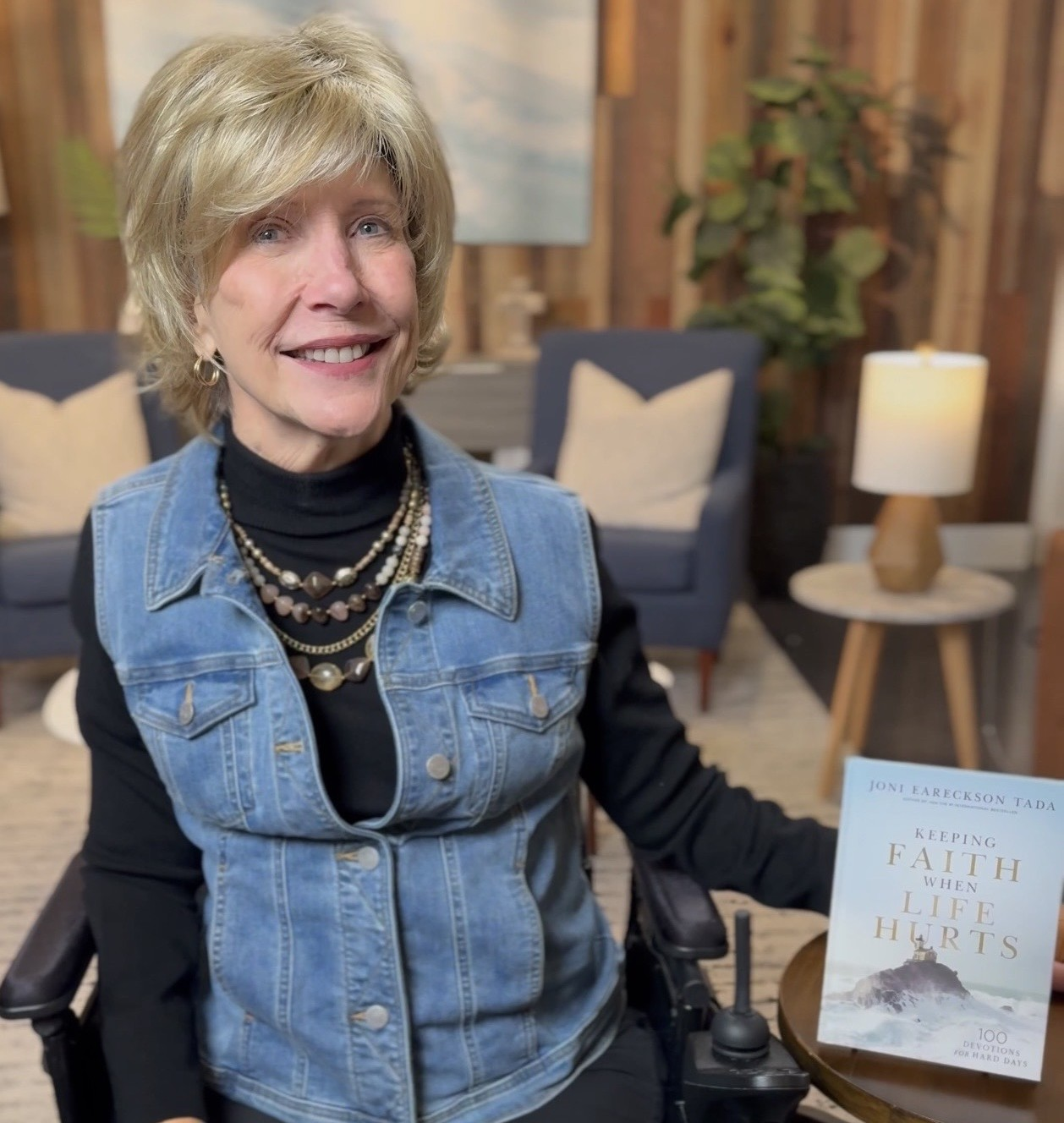 Joni Eareckson Tada beside her book Keeping Faith When Life Hurts in a cozy living room setting.