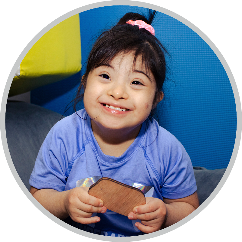 A young girl with Down Syndrome holding a wooden block.
