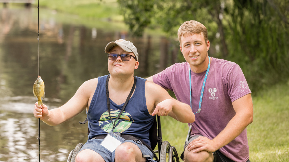 A camper shows off a fish he caught next to a volunteer as they pose for a photo