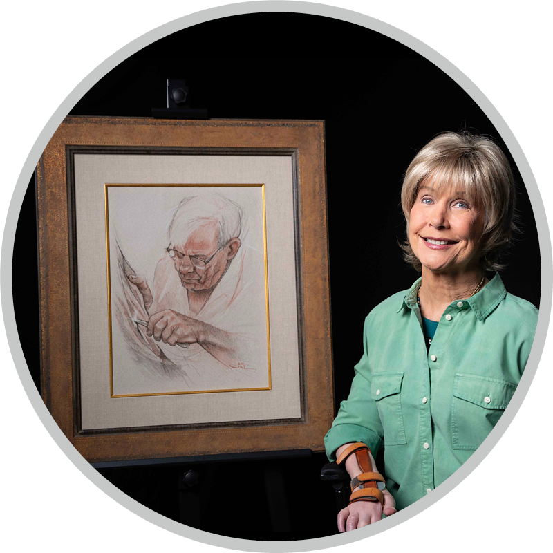 A picture of Joni smiling and sitting next to her drawing of her Father, titled, "My Father's Creation".
