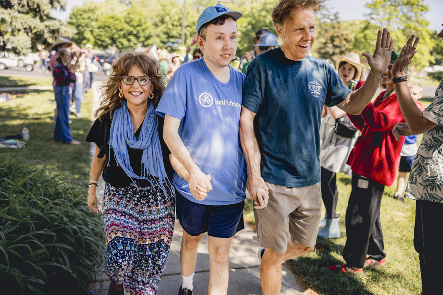 Yvonne, Ken, and their son Ryan hold hands while being warmly welcomed at Family Retreat, as Ken high-fives another person.