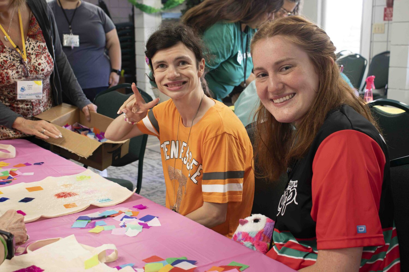 Katelyn poses with a peace sign next to a woman, with other people in the background.
