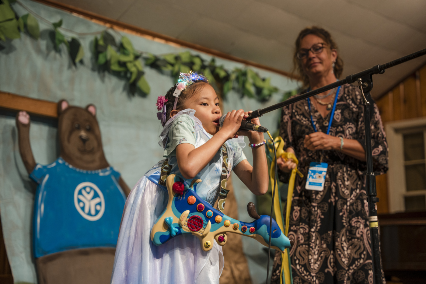 Isla on stage singing, with a woman standing next to her watching.