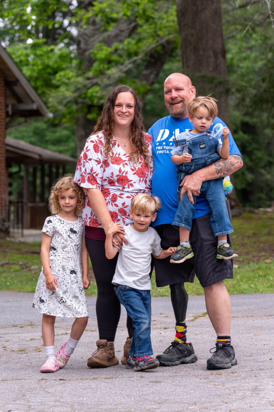Julia and Andy Butterworth are smiling and posing outdoors with their two sons and daughter, with trees and grass in the background.