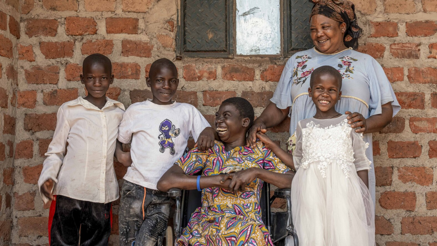 A woman in a wheelchair smiling with her family beside her, all smiling for the camera.
