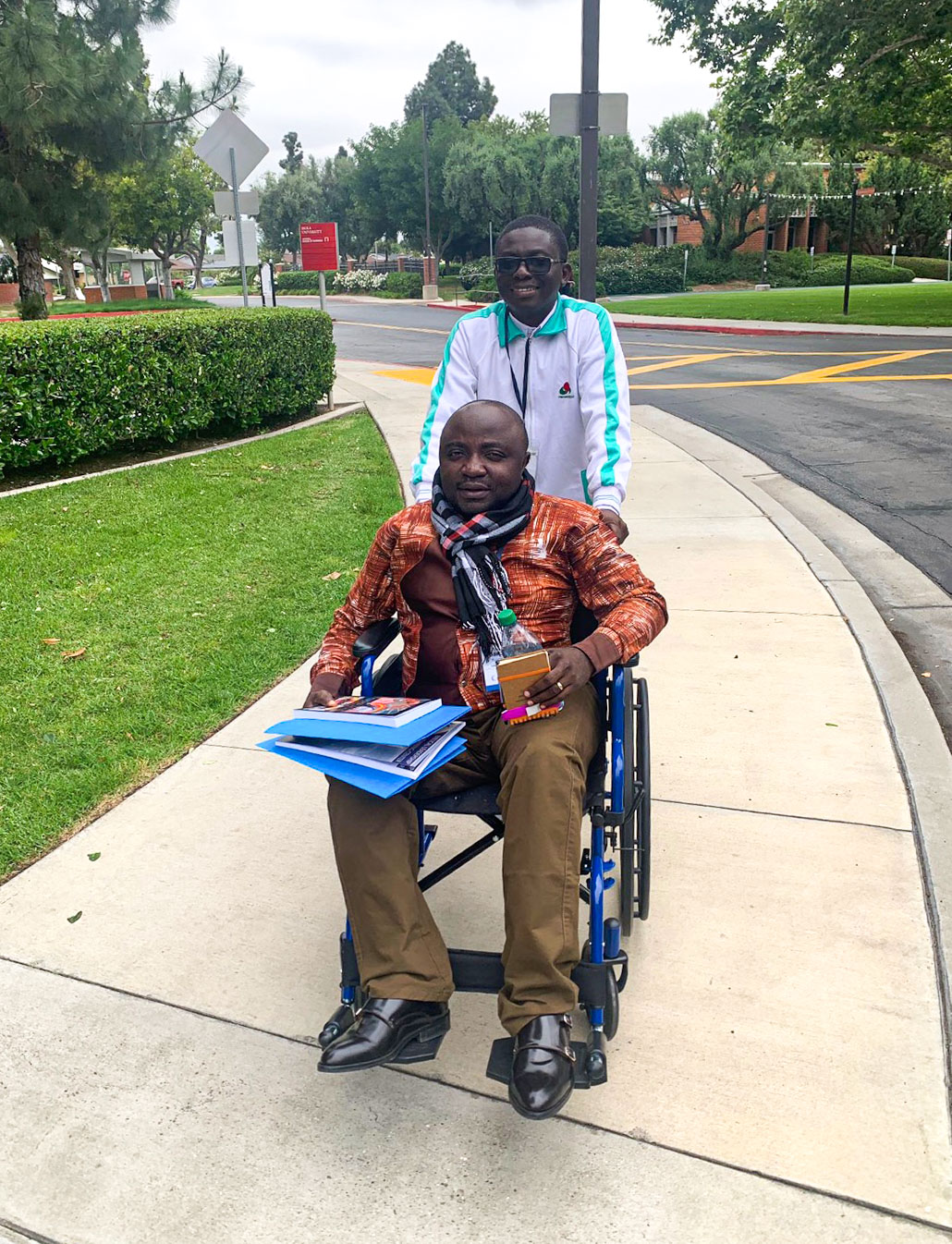 Daniel Kyungu in a wheelchair with a man pushing him.