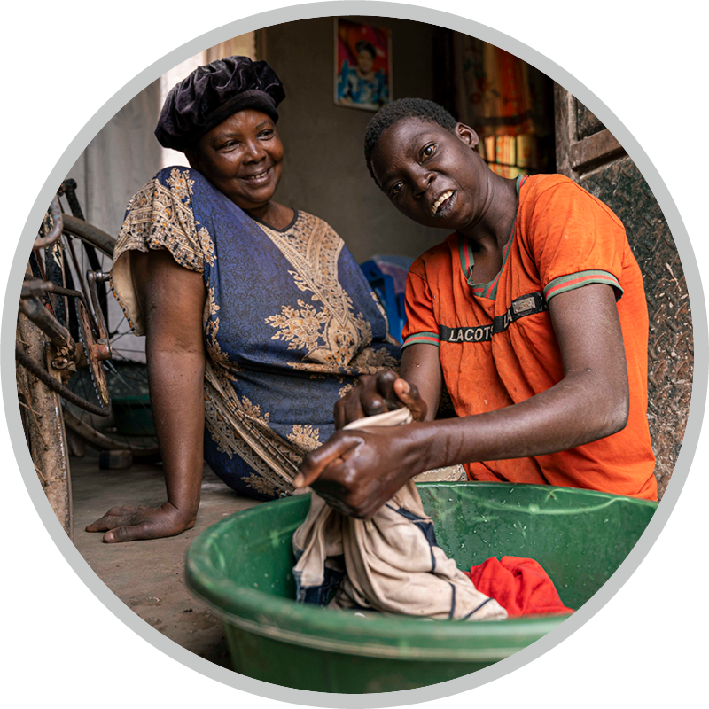 Fiona washing her clothes with a woman next to her. 
