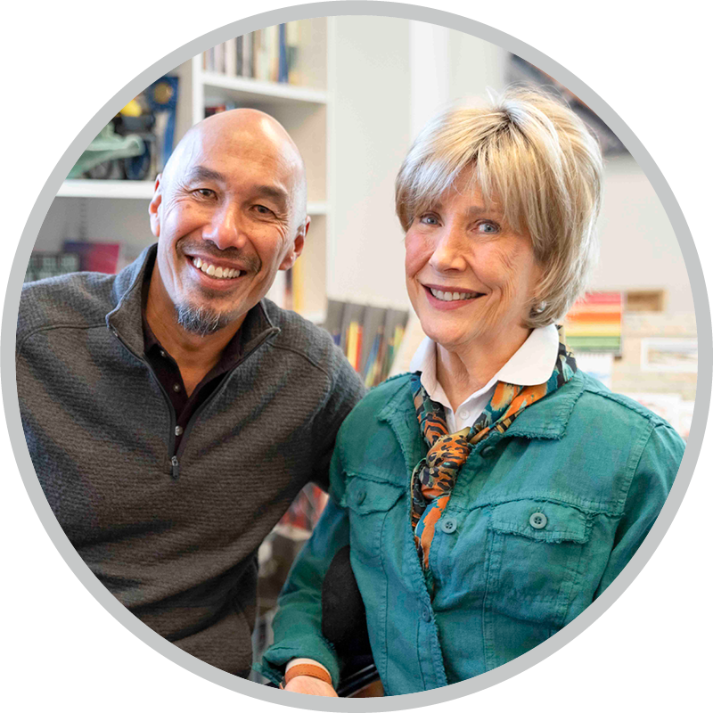 Francis Chan and Joni Eareckson Tada smiling together in Joni’s art studio, with teary eyes, surrounded by art supplies and framed artwork in the background.
