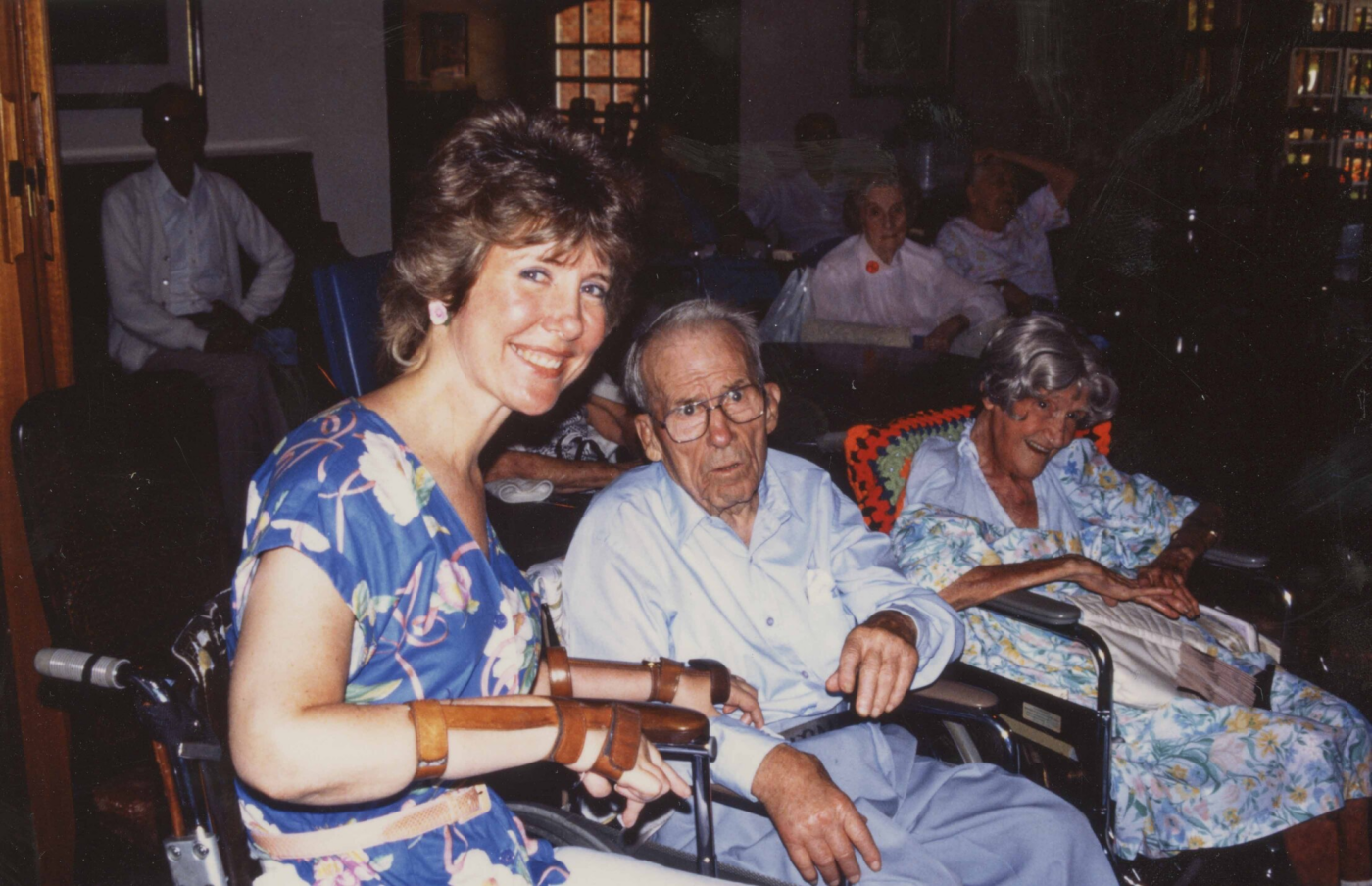 Joni Eareckson Tada in her wheelchair beside her father, John Eareckson, who is seated in a wheelchair, with other elderly people in wheelchairs in the background.