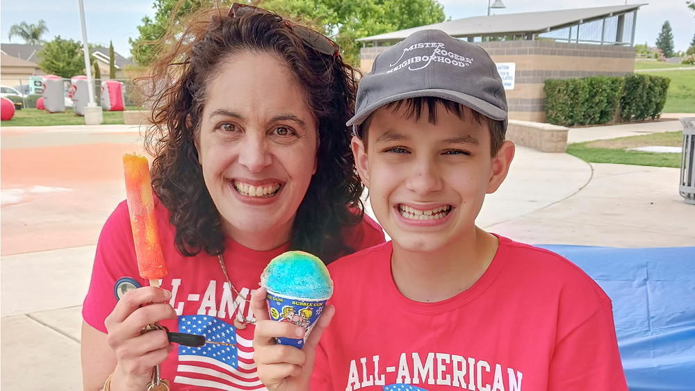 A mother and her son holding a popsicle and snow cone pose for a photo